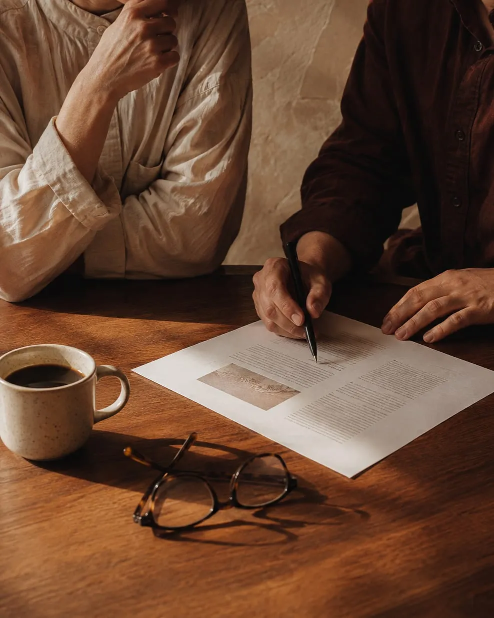 Two people at a table, one listening while the other writes on a printed page.